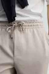 Pantalón jogger color beige de tejido transpirable y elástico con cintura elástica ajustable con cordón, bolsillos frontales y bajo con vuelta.