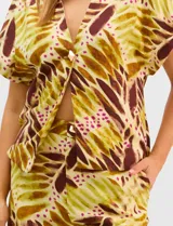 Conjunto de dos piezas confeccionado en mezcla de algodón y lino, con estampado abstracto en tonos verde y borravino. Incluye una blusa de manga corta con escote en V y cierre frontal con un botón, y un pantalón de tiro alto y pierna recta con bolsillos laterales.