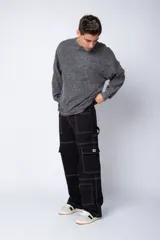 Pantalón tipo carpintero de corte relaxed fit y tiro medio, confeccionado en denim negro con costuras a contracolor en blanco. Presenta múltiples bolsillos cargo laterales, un bolsillo con cierre en la parte inferior y presillas utilitarias.