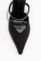 Sandalias tipo mule de tela negra con punta fina y taco fino forrado. Presenta una tira fina en el empeine decorada con strass y elástico lateral para mayor ajuste.