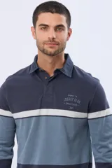 Remera polo de manga larga con diseño de bloques de color horizontales en tonos azul, verde y marrón. Presenta cuello clásico, cierre frontal con botones y bordado en el pecho. Cuenta con puños elásticos acanalados.