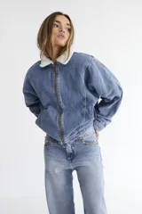 Campera bomber de denim azul con cierre frontal y cuello de corderito sintético. Presenta un diseño holgado con mangas amplias y forro interior de corderito.