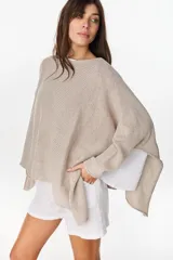Poncho oversize de tejido de punto con hilos de lurex, color crudo, escote bote y aberturas laterales.