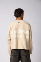 Buzo oversize de corte boxy, confeccionado en algodón rústico de alto gramaje en color beige. Presenta cuello redondo con borde crudo, mangas largas y una estampa frontal con el texto VCP delimitado por líneas horizontales blancas.