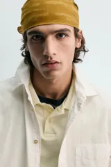 Camisa blanca de algodón con corte relajado, cuello solapa, manga larga con puño abotonado y bolsillo de plastrón en el pecho. Presenta bajo asimétrico con aberturas laterales y cierre frontal de botonadura.