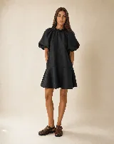 Vestido corto negro de lino 100% natural, con silueta amplia y relajada, cuello fruncido con volado sutil, mangas cortas abullonadas y faldón con volado en el bajo.