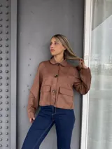 Campera corta de gamuza color marrón, con cuello clásico, cierre frontal con botones y dos bolsillos delanteros con solapa.