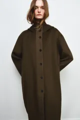 Parka oversize de corte recto confeccionada en tejido con mezcla de lana en color verde oliva. Presenta cuello alto con capucha, cierre frontal con botones y bolsillos laterales. Incluye detalles en tejido acolchado a contraste en la solapa frontal y puños.