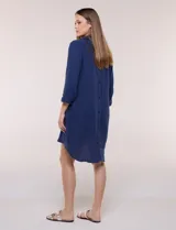 Vestido corto blanco de algodón, marca Dash, con cuello camisero, escote en V y bolsillos laterales. Presenta mangas tres cuartos y calce holgado con ruedo irregular.