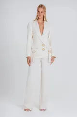 Blazer color marfil de corte estructurado, con solapas clásicas, cierre frontal de dos botones decorativos con detalle de piedra y bolsillos con solapa y correas laterales ajustables.