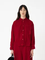 Camisa roja de terciopelo con corte cuadrado oversize, bolsillo delantero y botones dorados en cuello y puños.