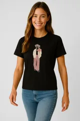 Remera negra de algodón con cuello redondo y manga corta. Presenta un estampado frontal de una figura humana con un abrigo beige, pantalón a rayas rosadas y un lazo rosado en el cuello, con detalles de lentejuelas.