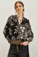 Camisa de viscosa negra con estampado floral en blanco, escote en V con lazo, cuello mao fruncido y mangas largas abullonadas con puños elásticos.