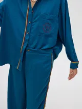 Pantalón de corte holgado y tiro alto con caída recta, color azul petróleo. Presenta una franja lateral decorativa en tonos rojo y amarillo que recorre la pierna, a juego con la camisa de la misma línea.