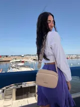 Bandolera de símil cuero color verde oliva, con diseño de dos compartimentos con cierre y correa ajustable de tela con patrón geométrico.