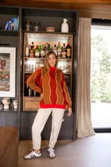 Sweater de punto con cuello alto, diseño geométrico con rayas diagonales en tonos naranja, marrón y blanco.