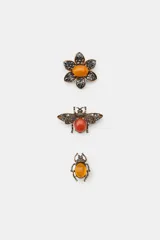 Set de tres broches metálicos con acabado envejecido. Incluye un broche en forma de flor con piedra central naranja, un broche en forma de abeja con piedra central rojiza y un broche en forma de escarabajo con piedra central ámbar. Todos los modelos cuentan con incrustaciones de cristales brillantes y cierre de imperdible.