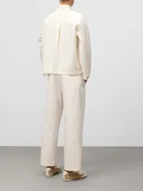 Camisa de corte recto en color crudo, con cuello chimenea y cierre frontal de botones. Presenta mangas largas con abertura y botón en los puños, canesú delantero y bolsillos de plastrón en el pecho con logo bordado. Confeccionada en una mezcla de fibras con tacto suave y acabado brillante.