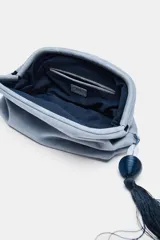 Bolso de mano tipo pouch de ante color celeste, con cierre imantado, bolsillo interior con cremallera y detalle colgante de borla con piedra.