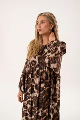 Vestido midi de corte holgado con estampado animal print en tonos marrones y beige. Tiene cuello redondo con lazo, mangas largas abullonadas y falda amplia con volantes. Incluye cinturón marrón con tachas.
