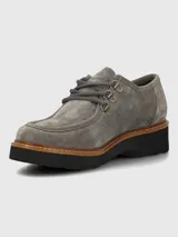 Zapato de estilo robusto confeccionado en descarne color gris, con diseño de cordones, ojales metálicos y suela gruesa de goma en color negro con detalle de vira en tono madera.