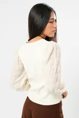 Blusa color manteca de cuello redondo y mangas largas abullonadas con puños elásticos.