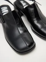 Zuecos de cuero vacuno con acabado en charol, color beige. Presentan un diseño clásico con taco cuadrado de madera de 5 cm y correa trasera ajustable con hebilla metálica.