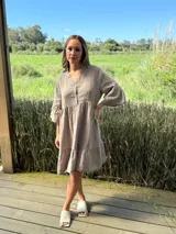 Vestido corto de lino color beige, con cuello mao, escote abotonado, mangas 3/4 con volados y ruedo con volado.