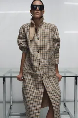 Trench reversible de Zara Woman Collection con diseño de cuadros en tonos beige, negro y tostado. Cuenta con cuello de solapa, cierre frontal con botones oscuros y bolsillos delanteros diagonales.