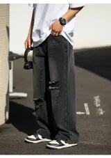 Jean de corte ancho y holgado, color negro lavado con efecto desgastado y roturas visibles en la parte delantera de las piernas. Presenta cinco bolsillos.