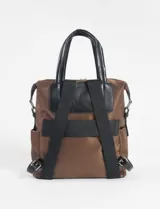 Mochila de diseño versátil en color marrón, confeccionada en tela técnica con detalles en cuero vegano negro. Cuenta con manijas superiores para llevar como bolso, correas ajustables, bolsillo frontal con cierre y compartimento principal con cierre.