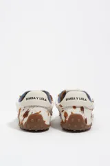 Zapatilla de perfil bajo confeccionada en serraje vacuno con estampado de manchas tipo animal print vacuno. Presenta cierre de cordones, detalle de piel en el talón con logo y suela de goma con textura de tachuelas.