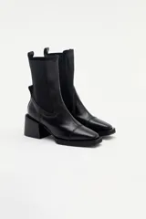 Bota tipo chelsea de cuero charolado color bordó, con caña media, elásticos laterales negros y taco cuadrado bajo.