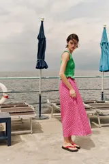 Falda midi con silueta evasé y estampado de cuadros en tonos fucsia y blanco. Presenta cintura elástica con lazo ajustable y detalle de borlas colgantes.