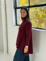 Sweater de punto color bordó con cuello alto tipo polera, diseño de corte evasé con costura central vertical y bajo asimétrico más largo en la parte posterior.