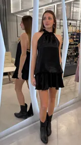Vestido corto negro de cuello halter con acabado satinado, espalda descubierta y falda evasé con volados.