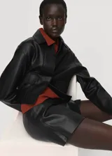 Falda pantalón corta de efecto piel color negro, de tiro medio con diseño cruzado y cierre de cremallera lateral.