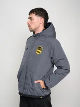Campera de abrigo corta negra con capucha y costuras en contraste color amarillo. Estampado del escudo del Club Atlético Peñarol en el pecho y en la espalda.