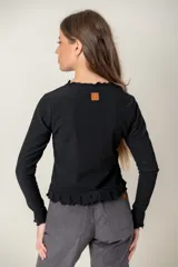 Polera de manga larga color negro, con textura acanalada, cuello redondo y terminaciones con volados en el cuello, puños y ruedo.