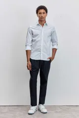 Camisa de manga larga con cuello clásico y cierre frontal de botones. Presenta un diseño de rayas verticales finas en tonos claros.