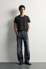 Jeans loose fit de hombre en denim de algodón color gris oscuro con efecto lavado. Presenta perneras con costuras giradas hacia los tobillos, tiro medio, cierre frontal con botones y bolsillos frontales con bolsillo cerillero.