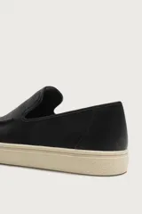 Mocasín casual de cuero negro con textura granulada, diseño sin cordones y suela de goma a contraste en color beige.
