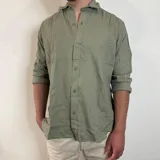 Camisa de manga larga confeccionada en lino, color blanco, con cuello clásico y cierre frontal de botones.