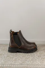 Botas tipo Chelsea de cuero con acabado vintage, diseño de caña media con paneles elásticos laterales y suela track robusta.