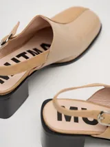 Zuecos de cuero vacuno con acabado en charol, color beige. Presentan un diseño clásico con taco cuadrado de madera de 5 cm y correa trasera ajustable con hebilla metálica.