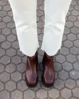 Botinetas de caña baja confeccionadas en cuero vacuno color chocolate, con paneles laterales en gamuza al tono. Presentan suela track de goma negra, cierre lateral interno y puntera redondeada.