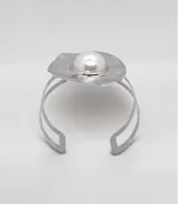 Brazalete rígido de diseño circular con acabado plateado texturizado e irregular, destacando una perla central grande. Presenta un estilo moderno y llamativo.