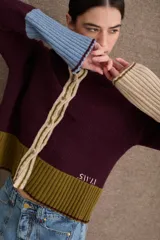 Cardigan de punto con diseño color block en tonos bordó, verde oliva y beige. Presenta cuello redondo con detalle en celeste, cierre frontal con botones y puños acampanados en color beige.