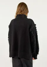 Sweater de punto color azul marino, con cuello alto, diseño de rombos en relieve y detalle de flecos en las mangas.