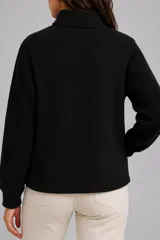 Abrigo negro de estilo bomber con cuerpo de tejido compacto y mangas de punto acanalado. Presenta cuello alto, cierre frontal con botones a presión y bolsillos laterales.